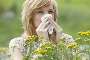 woman outside blowing her nose ragweed in front of her
