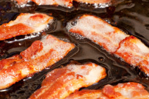 A bacon cooking detail, slices of bacon in fat