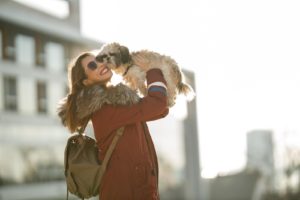 Portrait of a smiling young woman bonding with her cute Shih Tzu dog at the city.