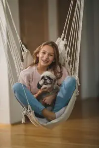 Shot of a cute smiling teenage girl swingigng with her cute dog and enjoying leisure time at her home.