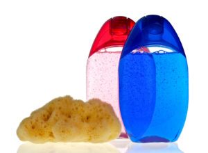 Blue and crimson transparent shampoo bottles with sponge on white background