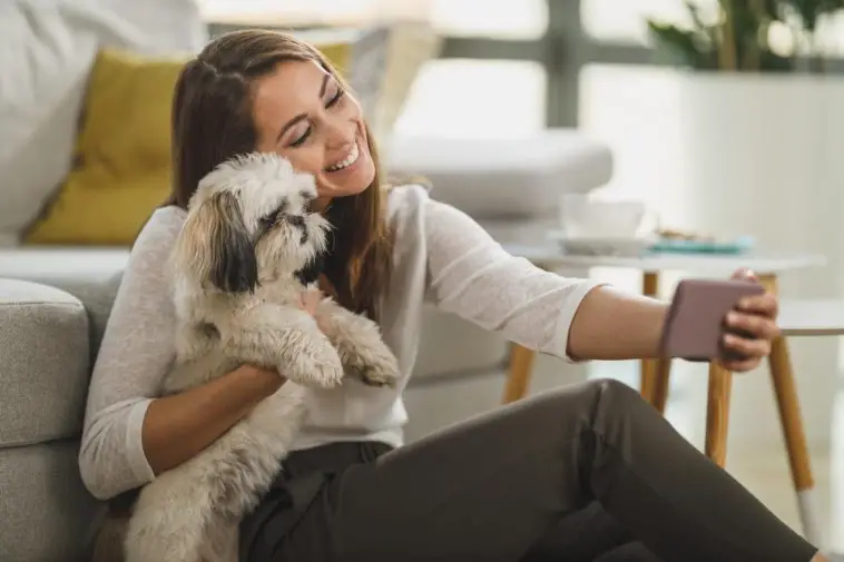 Shot of a cute young woman taking and selfie while relaxing with pet dog in her living room at the home.